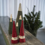 Hæklede keglenisser i rød og naturfarve og keglejuletræer i grønne nuancer står samlet på et træbord som minimalistisk julepynt.